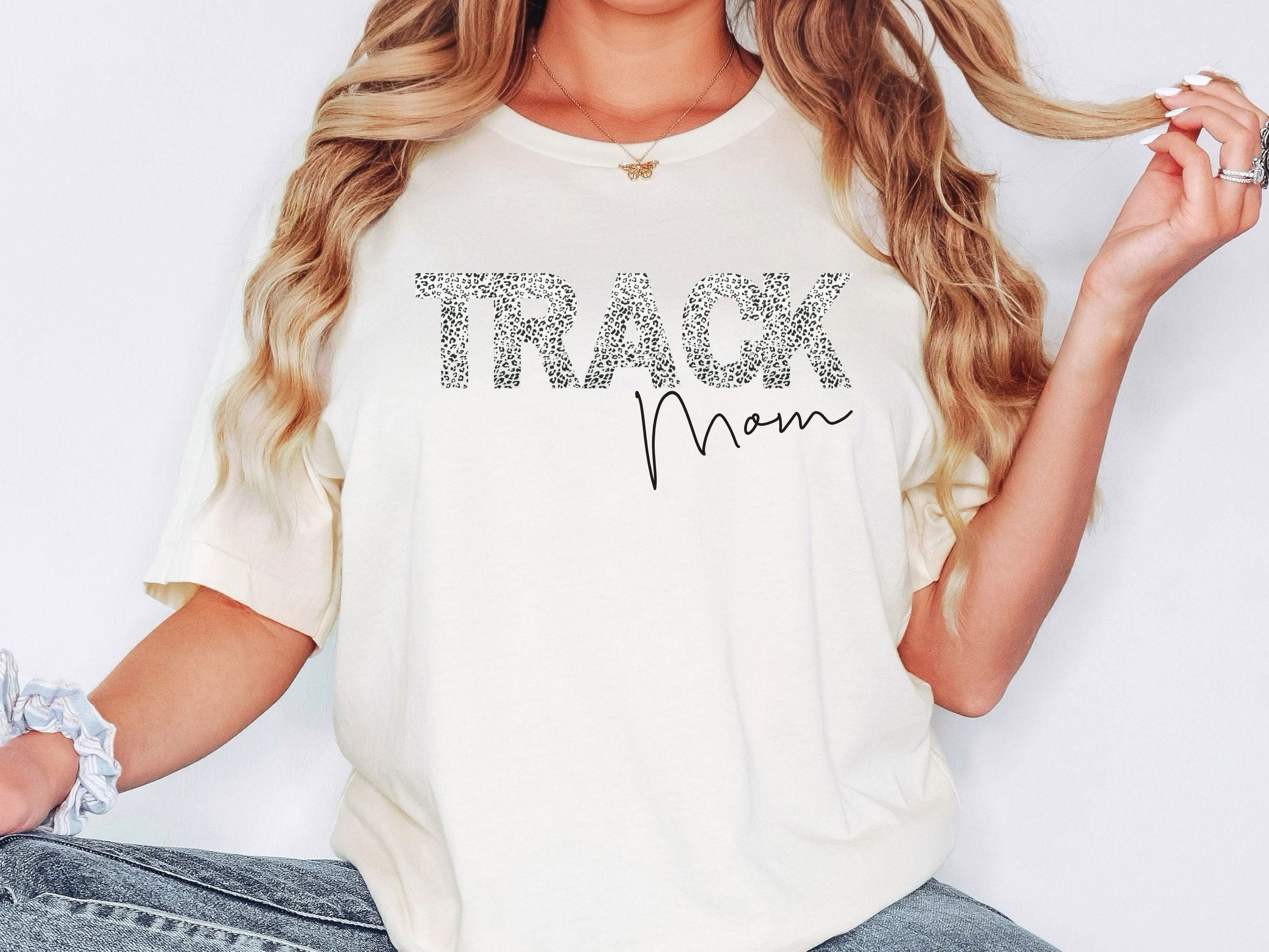 Woman wearing a white t-shirt with 'Track Mom' text on a plain background