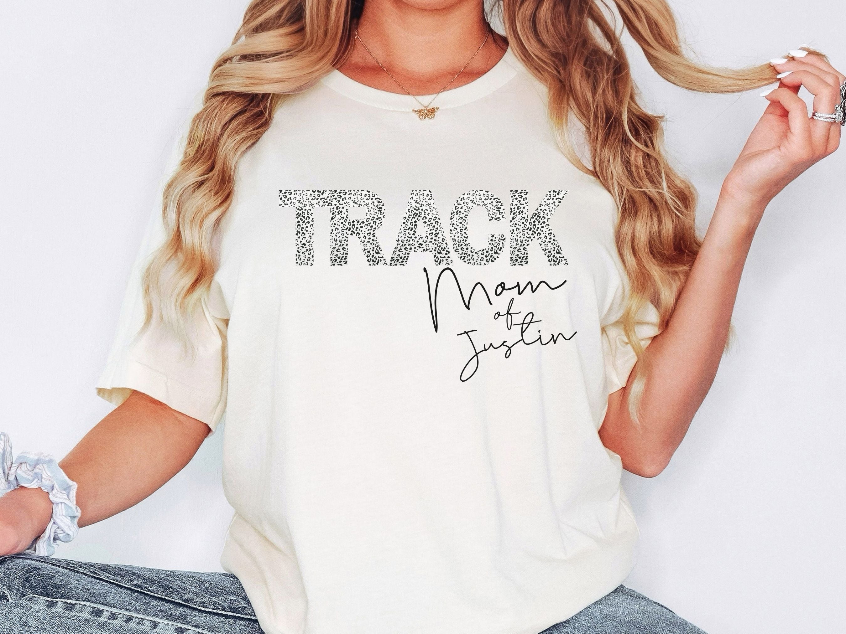 Person wearing a white t-shirt with 'Track Mom of Justin' text on a plain background