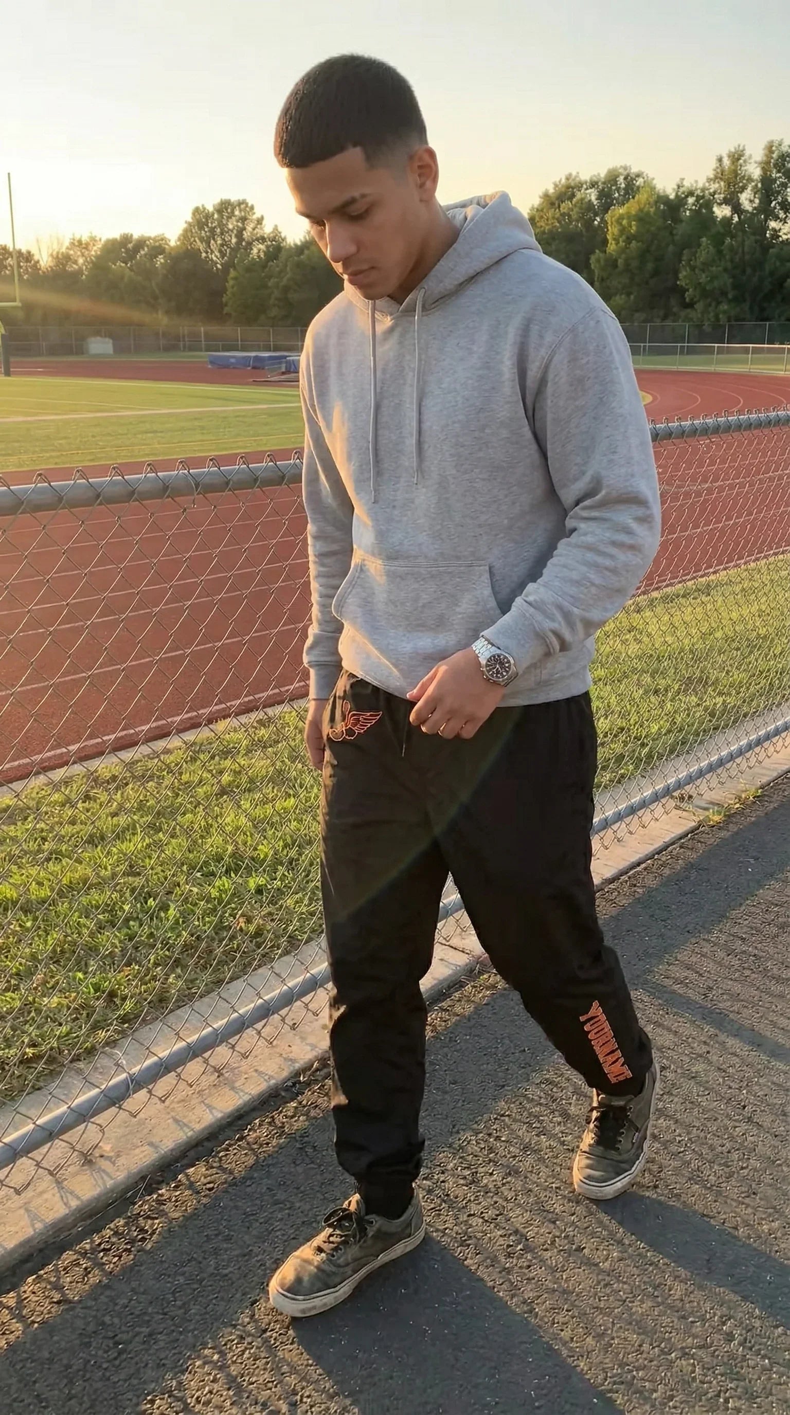 Person wearing a gray hoodie and black pants on a track field