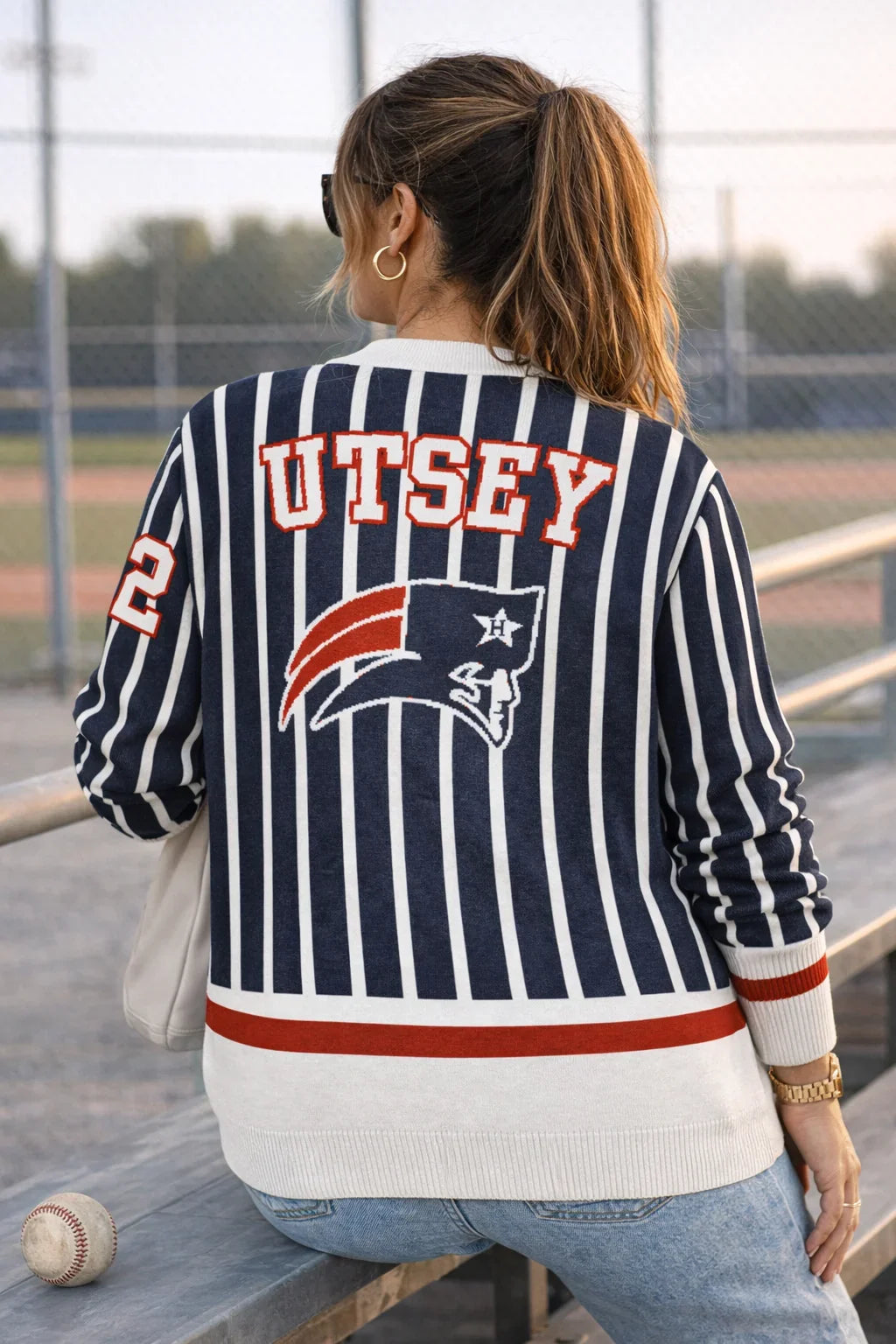 Woman in striped navy sports sweater with 'UTSEY' lettering at a baseball field bench