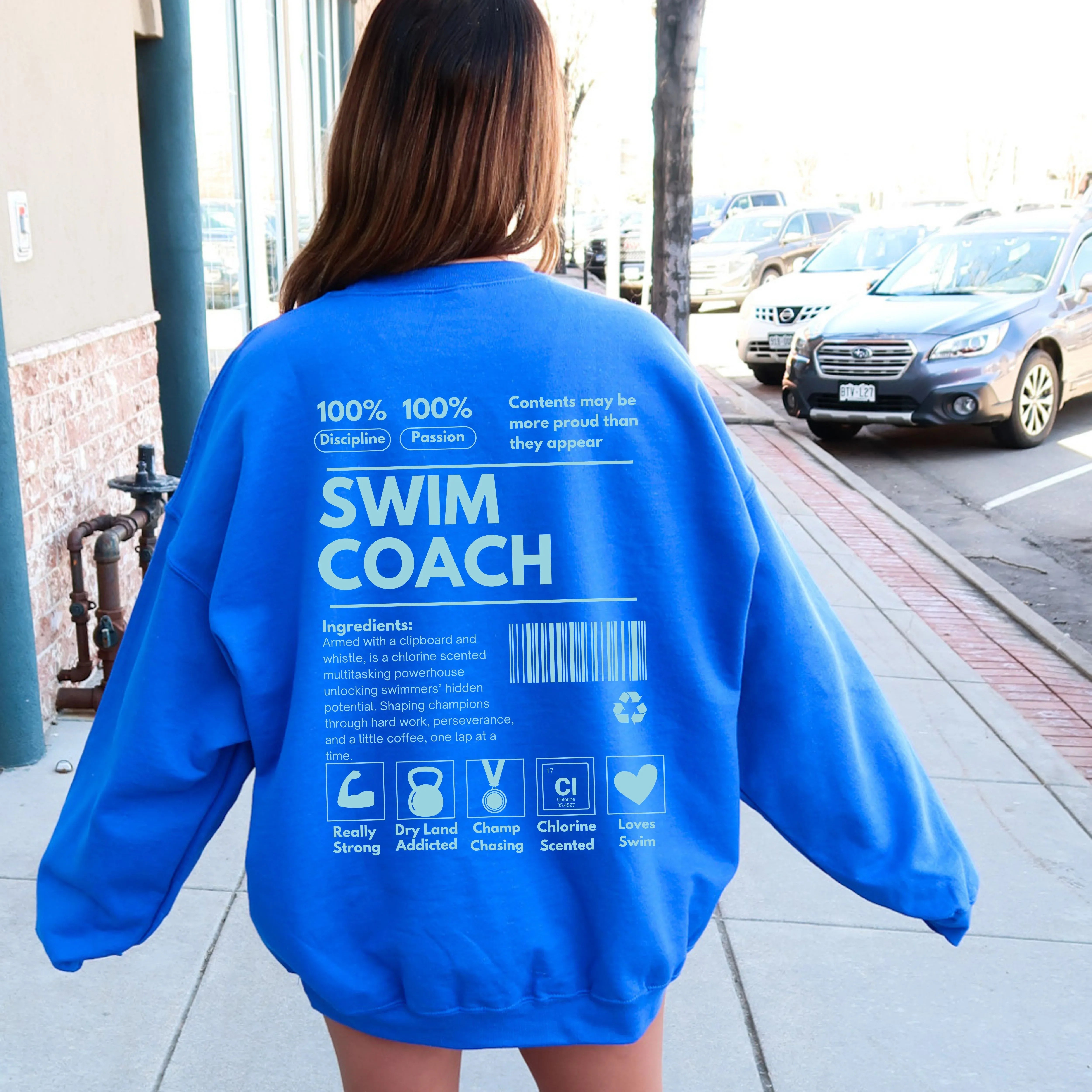 Person wearing a blue sweatshirt with 'SWIM COACH' text on the back, standing on a sidewalk.