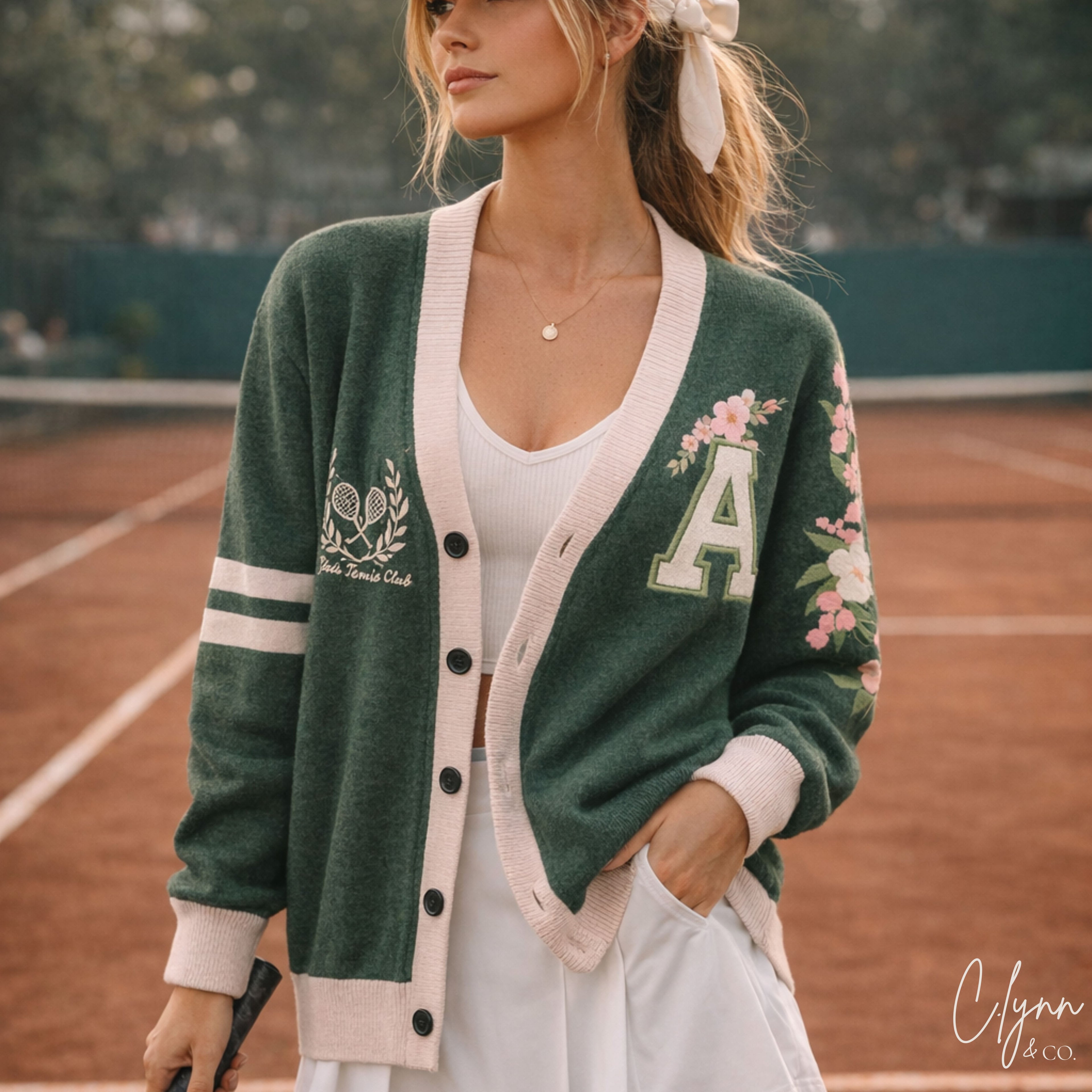 Woman wearing green varsity cardigan with floral embroidery and tennis motif on court