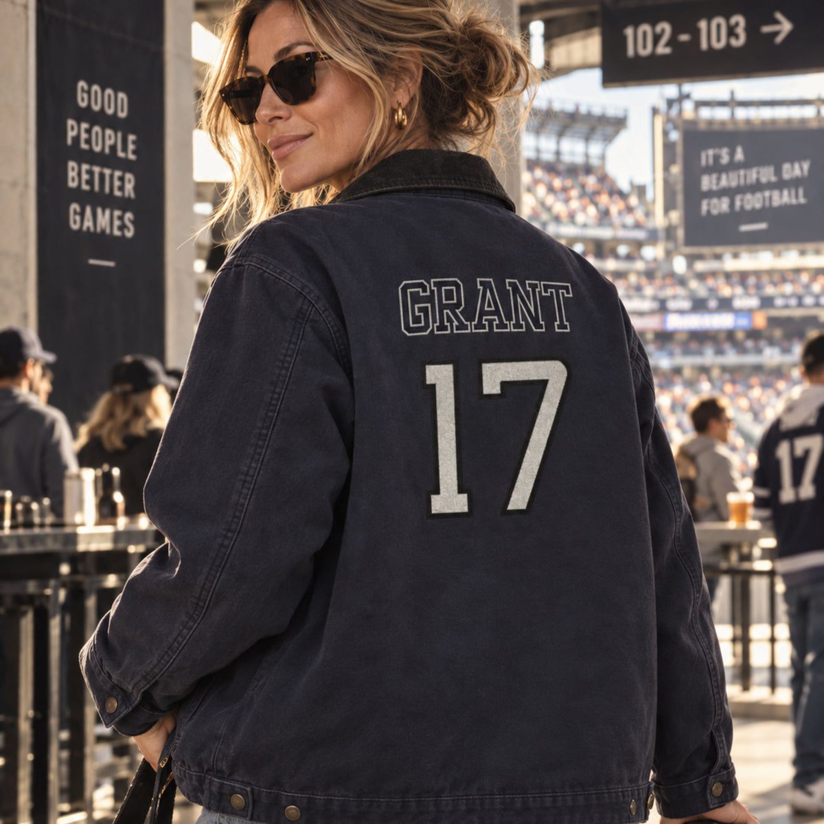 A woman at a stadium wearing a dark navy blue denim-style jacket with 'GRANT' and the number '17' printed on the back in white and gray.