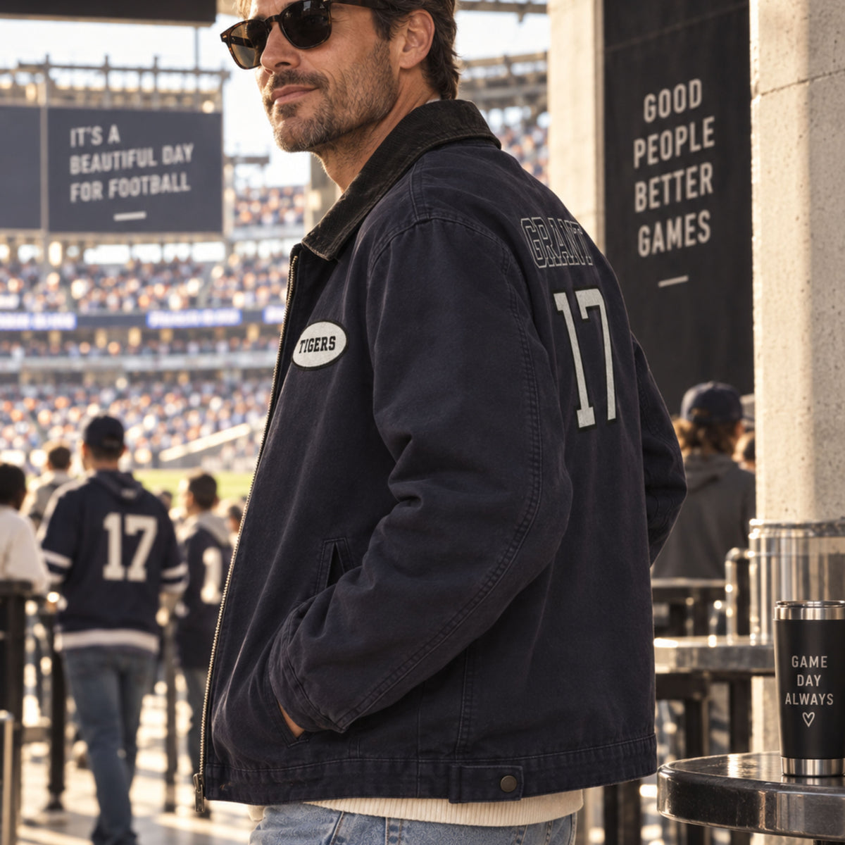 A man in a stadium wearing a navy blue jacket with 'SEMPER' and the number '17' on the back, along with a circular 'Tigers' patch on the chest.