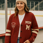 Woman in red varsity cardigan with 'MOM' lettering and knit beanie at ice rink