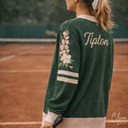 Woman in green varsity sweater with floral embroidery and 'Tipton' text on tennis court