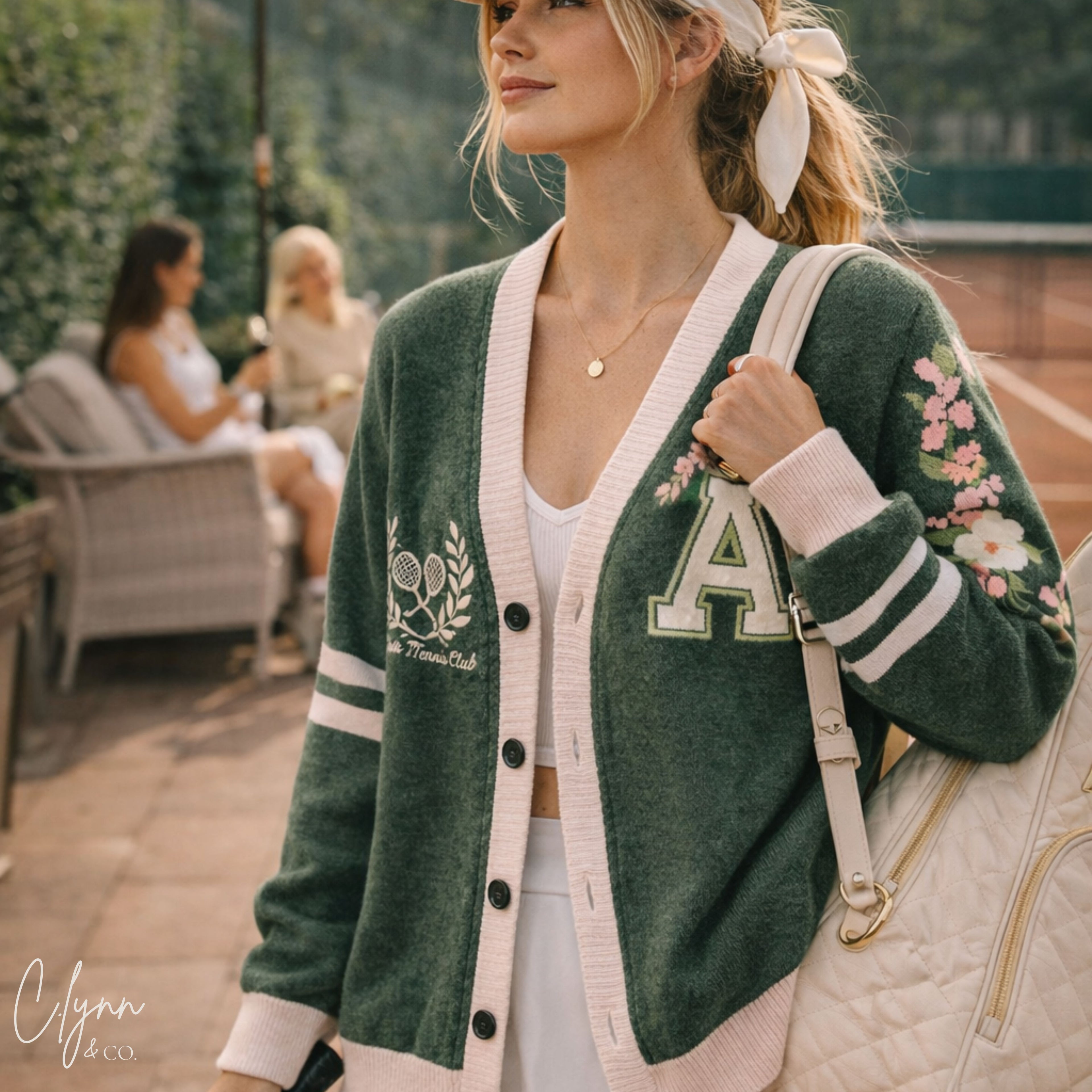 Woman in green varsity tennis club cardigan with floral details, on a tennis court