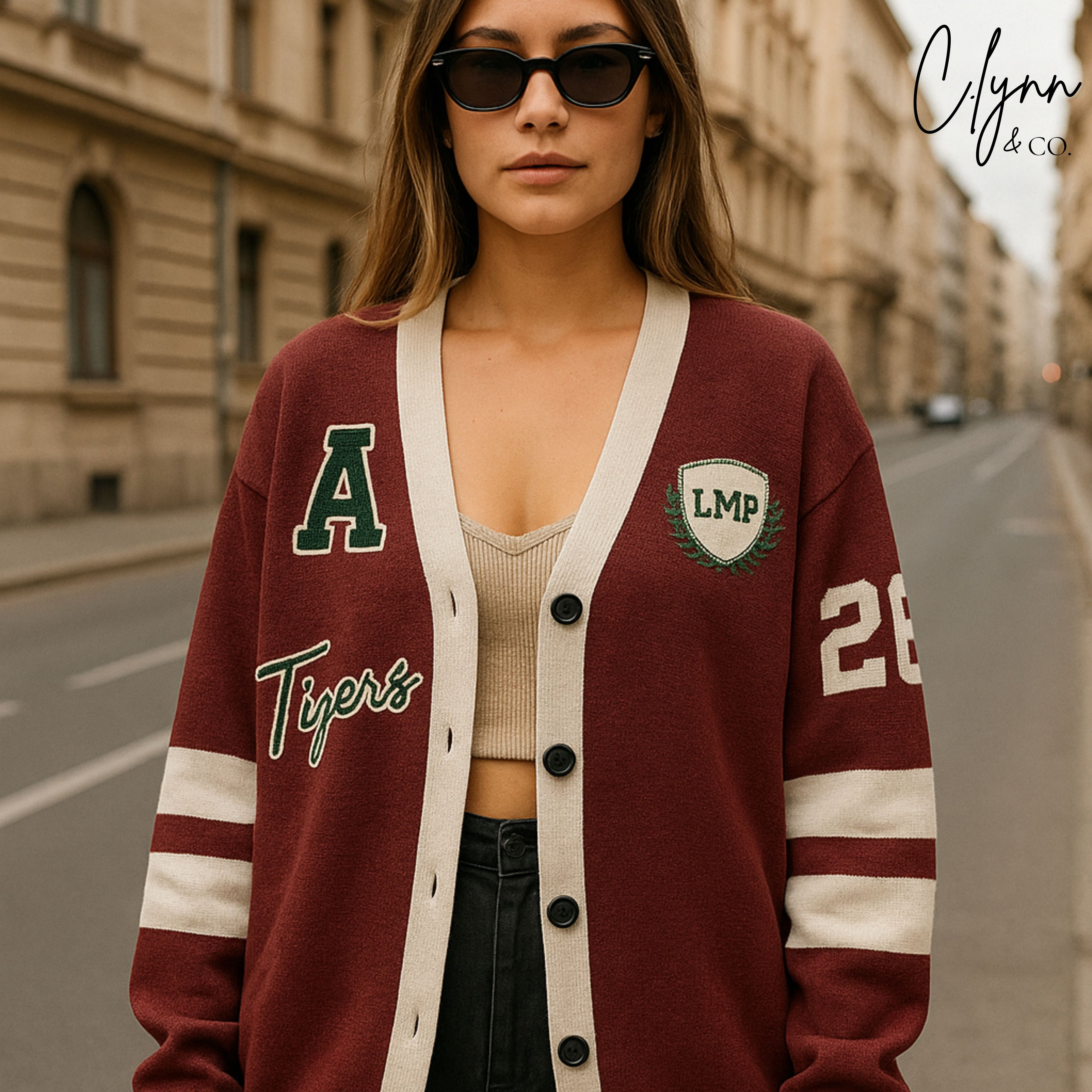 Woman wearing a maroon varsity cardigan with sporty letter patches and white stripes on sleeves.