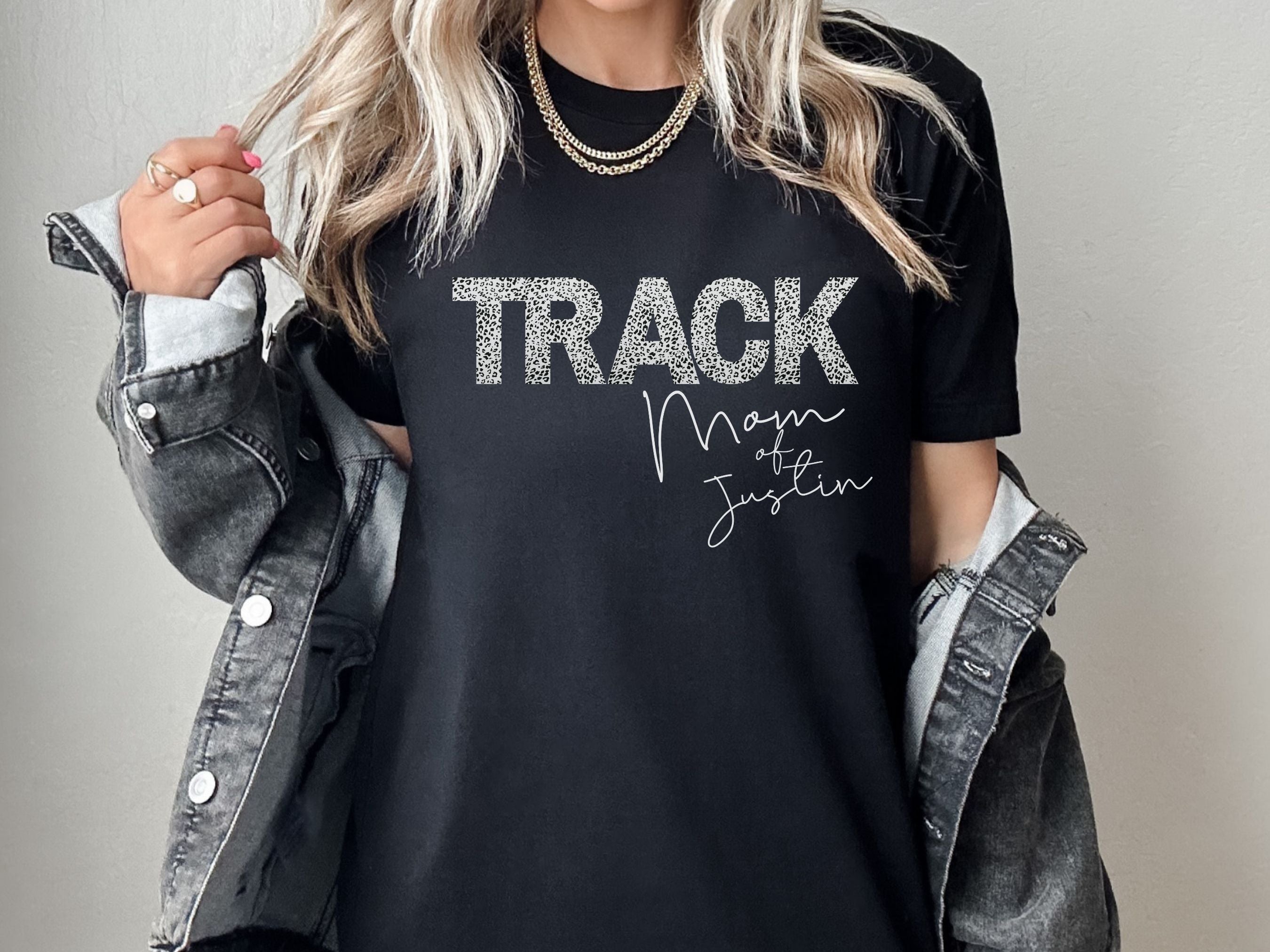 Person wearing a black t-shirt with 'TRACK Mom of Justin' text, holding a jacket.