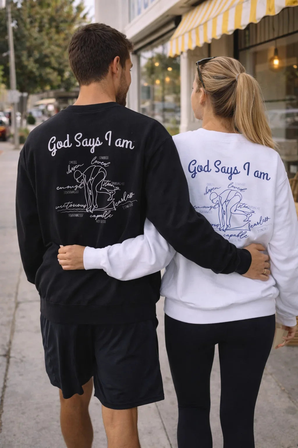 Two people wearing shirts with 'God Says I am' text, walking together on a sidewalk.