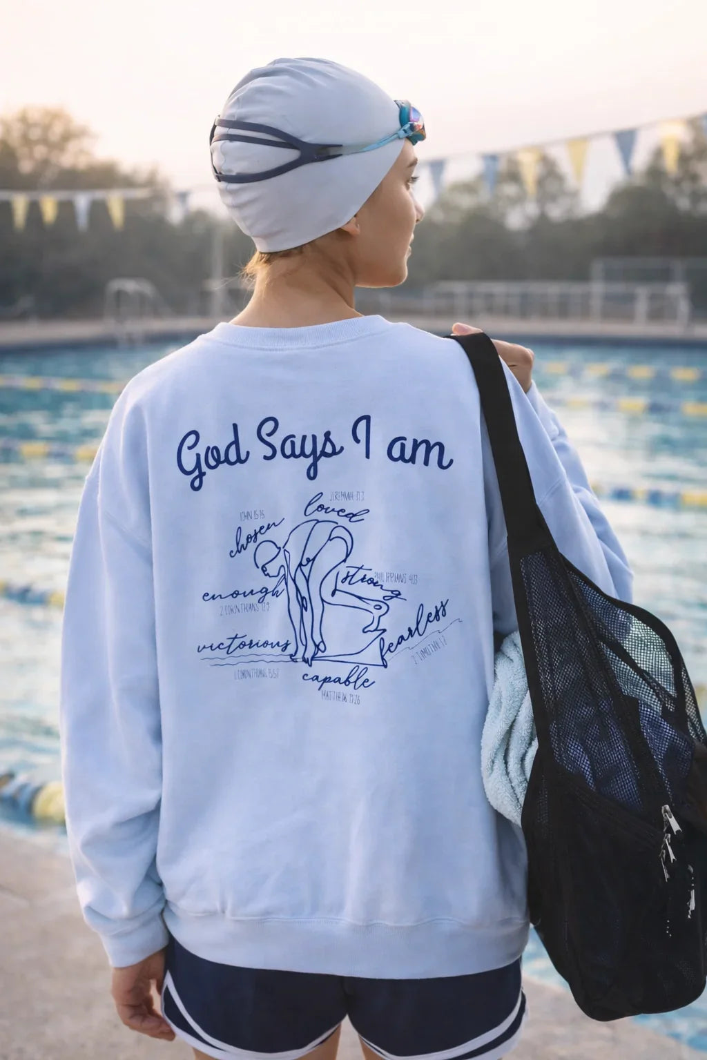 Swimmer on the pool deck in a light blue sweatshirt with text God Says I Am with a swimmer graphic faith based text