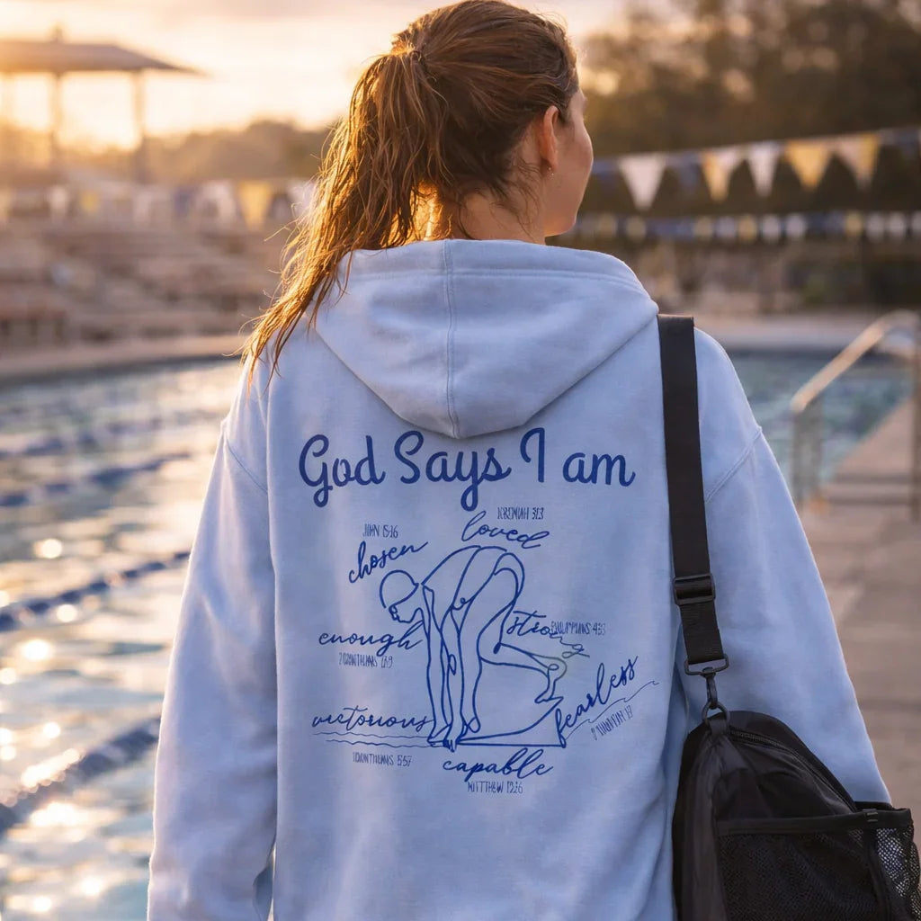 Person wearing a hoodie with text and graphics by a pool at sunset