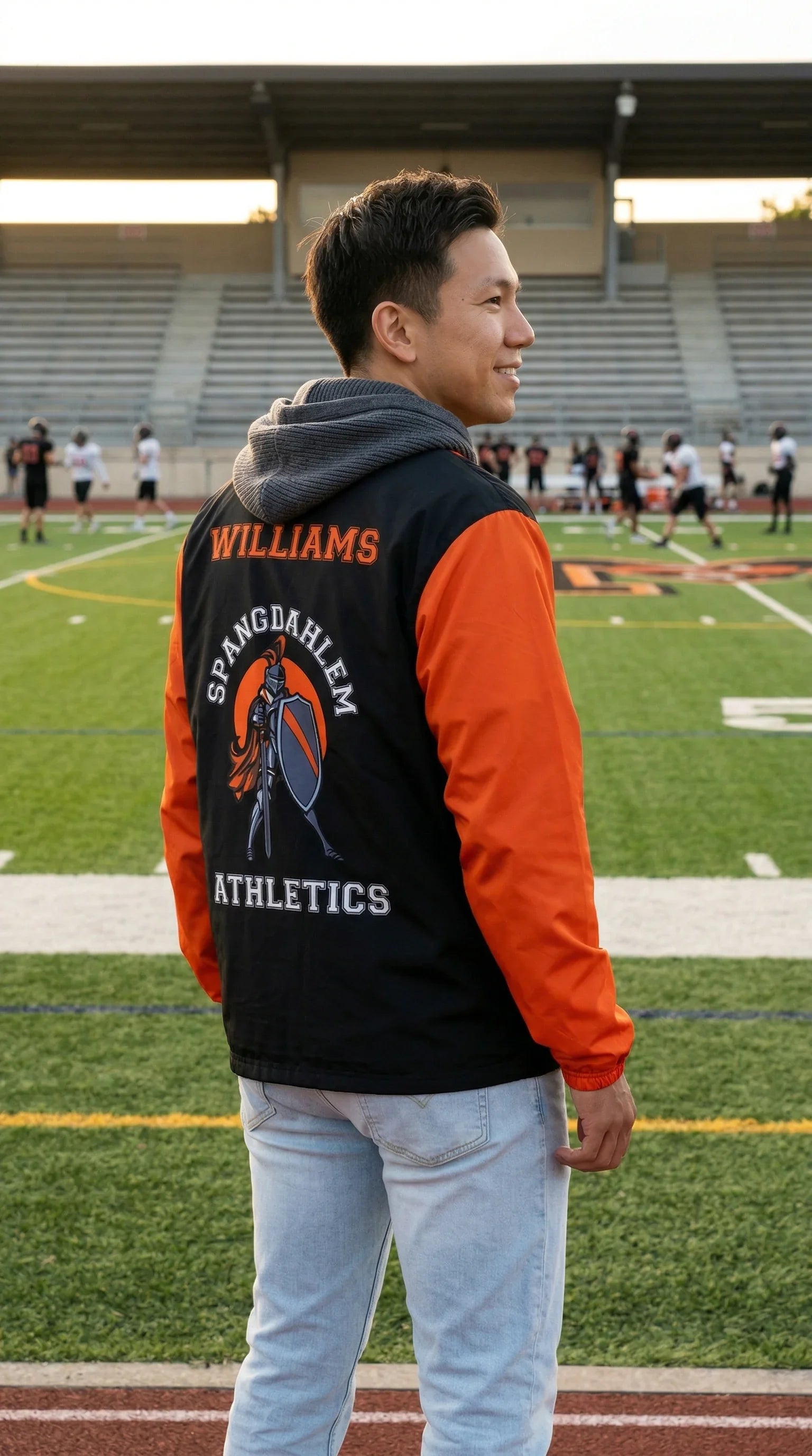 Person wearing a varsity jacket with 'Williams Spanaway Athletics' on a sports field.