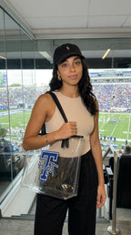 Woman holding a clear bag with a logo, standing in a stadium setting.