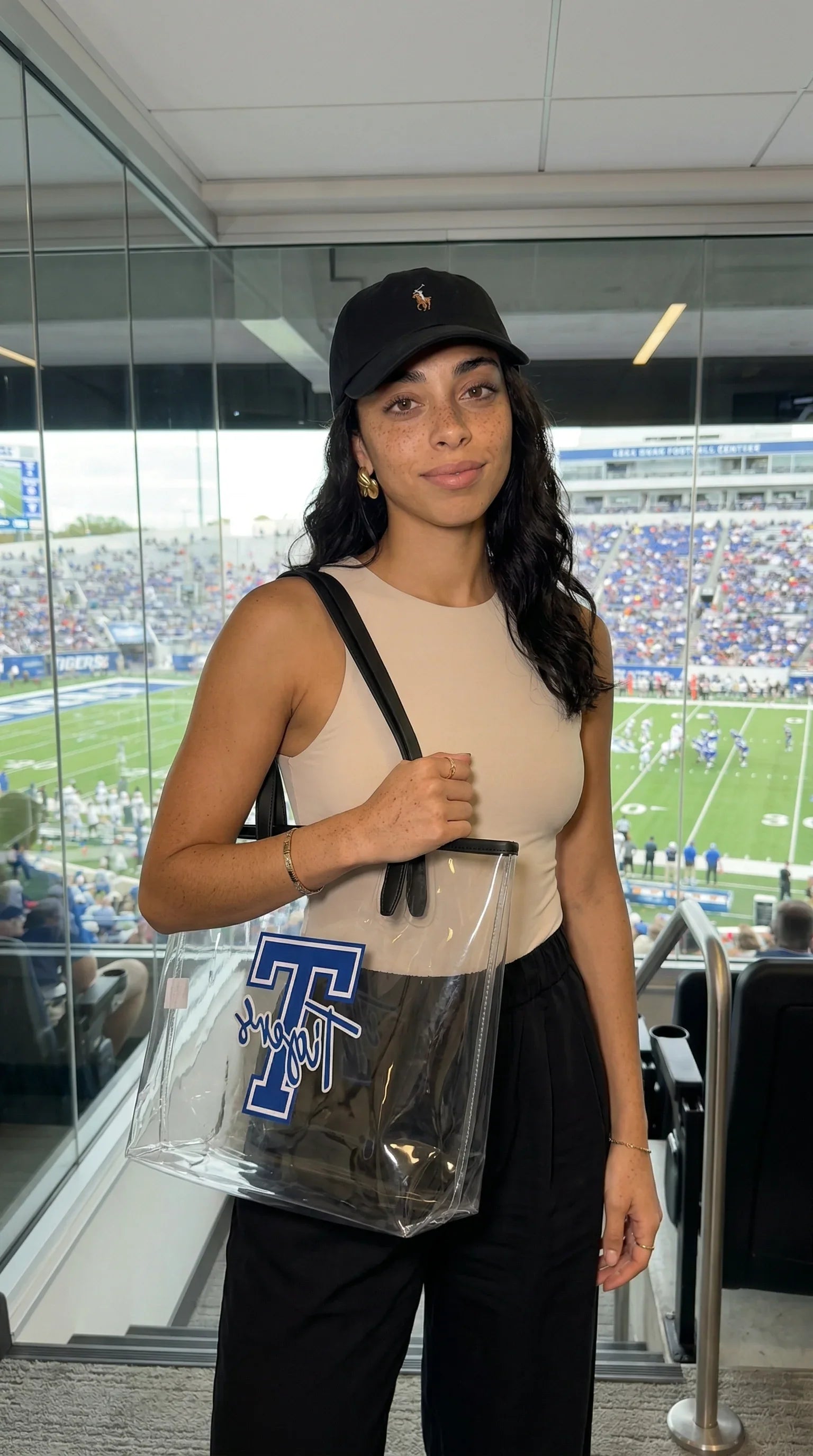 Woman holding a clear bag with a logo, standing in a stadium setting.