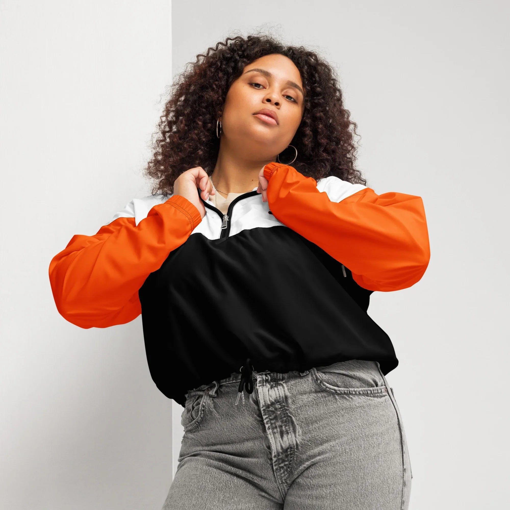 Woman wearing an orange and black jacket with gray pants on a light gray background