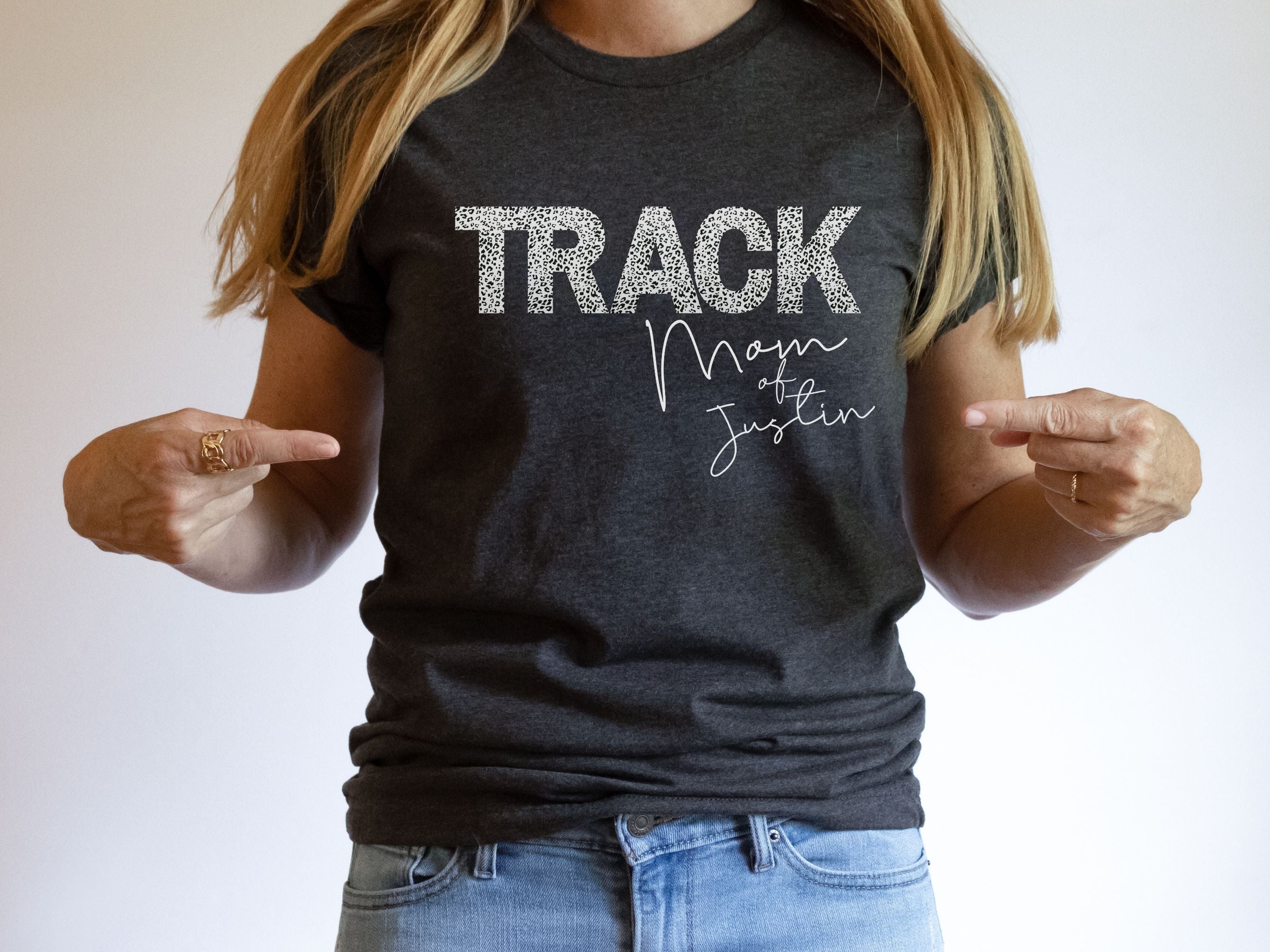 Person wearing a black t-shirt with 'TRACK Mom of Justin' text, pointing at the shirt.