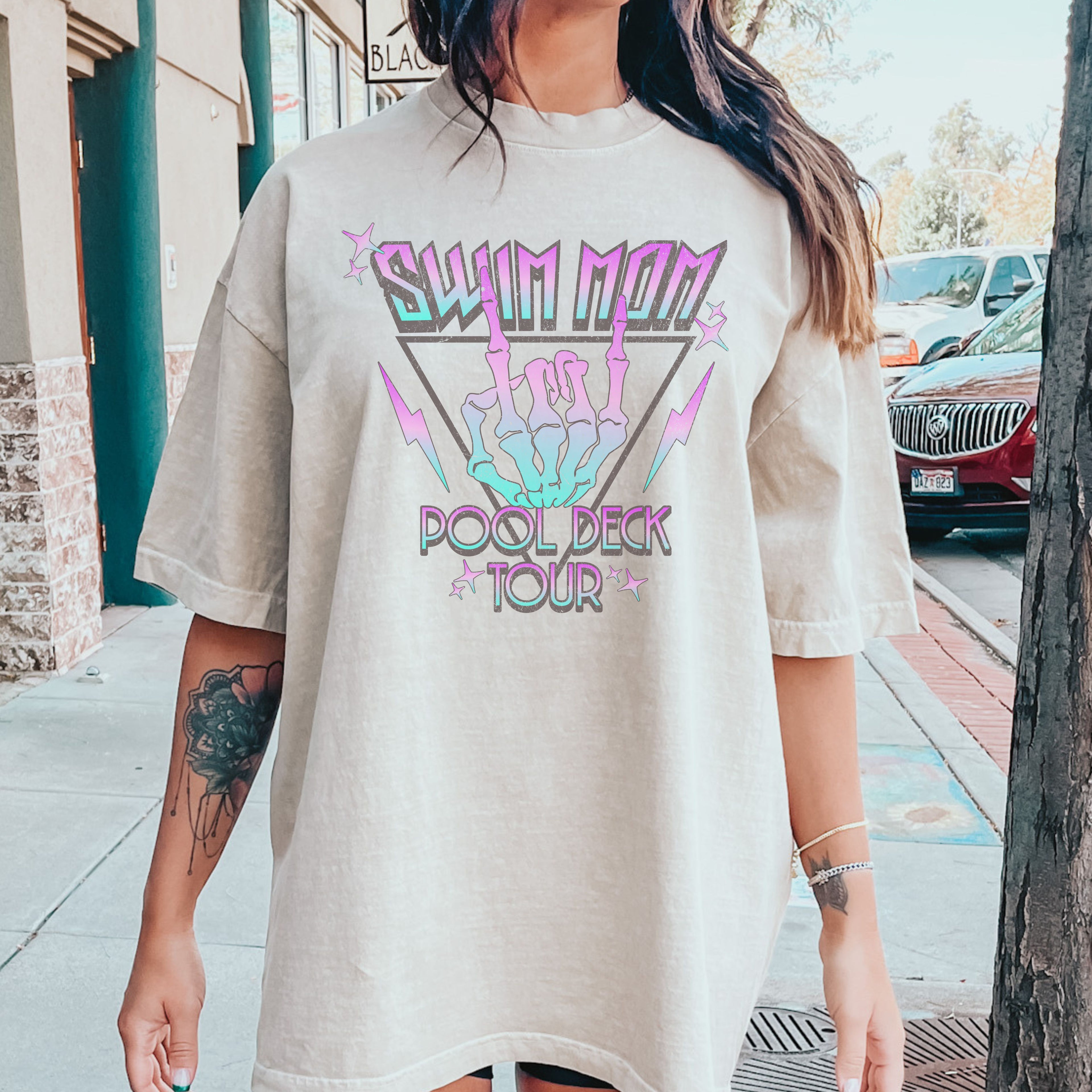Person wearing a beige t-shirt with colorful swim mom graphic design outdoors.