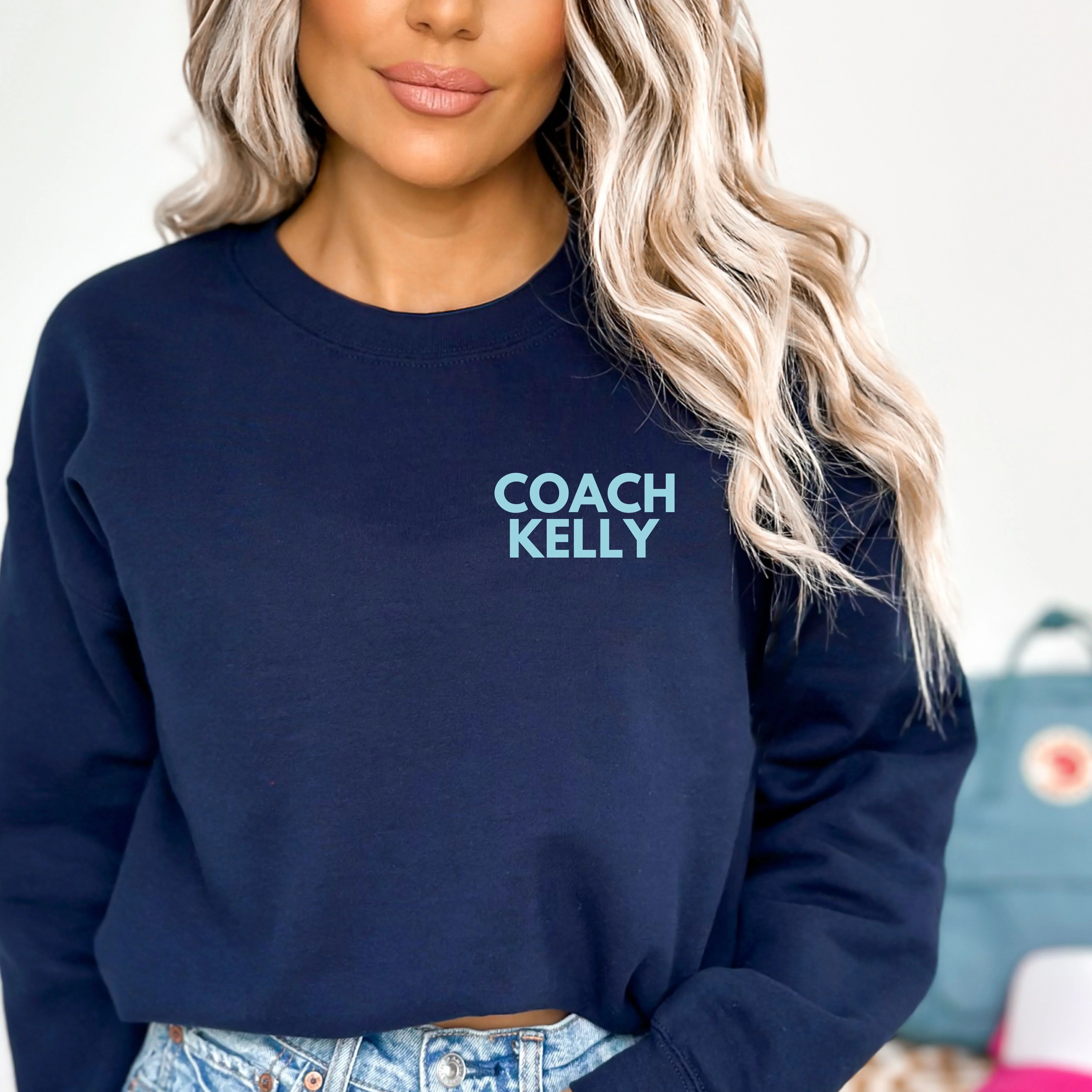 Person wearing a navy blue sweatshirt with 'COACH KELLY' text, blurred background
