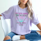 Person wearing a lavender t-shirt with colorful text design, sitting on a white chair.