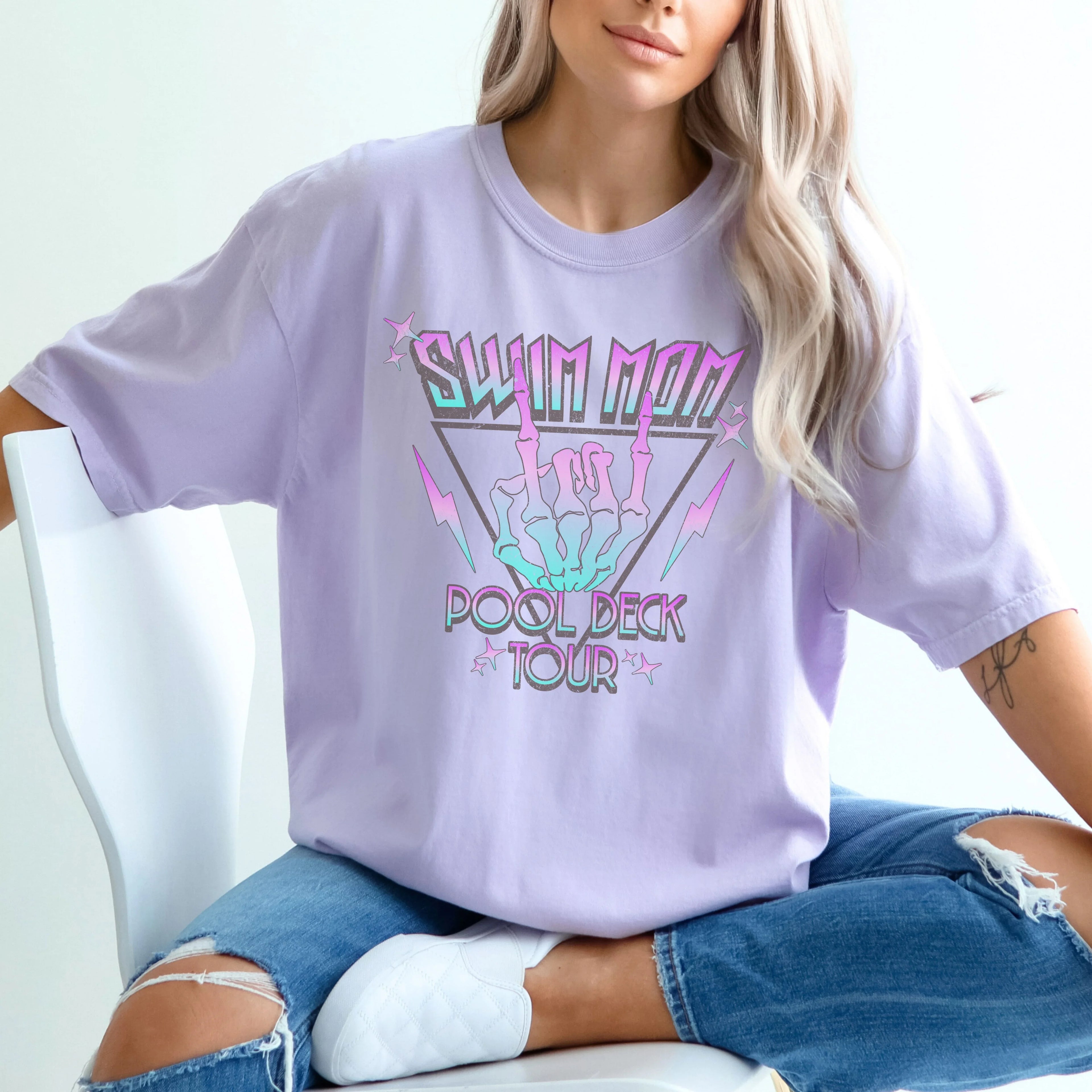 Person wearing a lavender t-shirt with colorful text design, sitting on a white chair.
