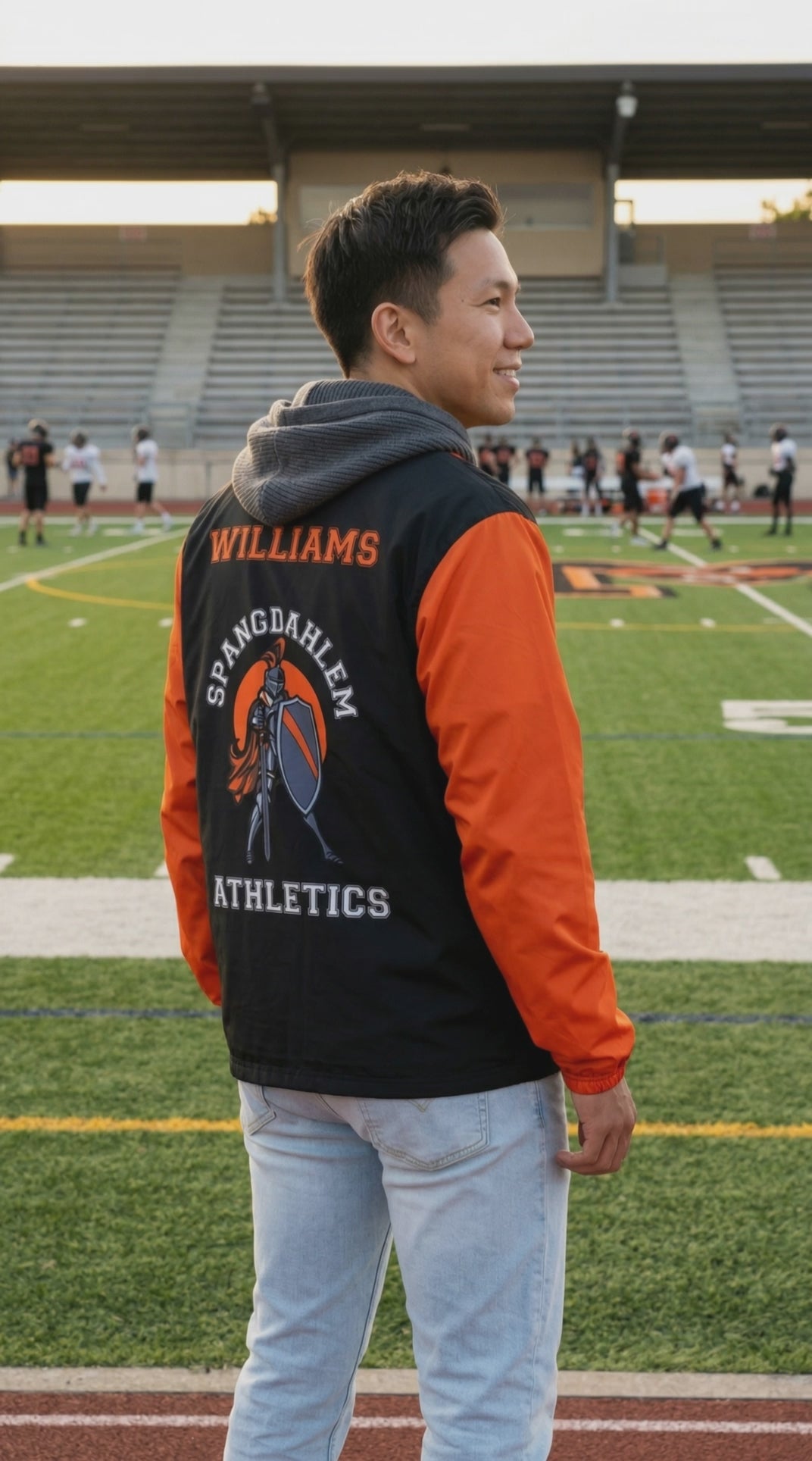Person wearing a custom Athletics windbreaker jacket on a sports field with other people in the background.
