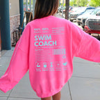 Person wearing a bright pink 'SWIM COACH' shirt outdoors.