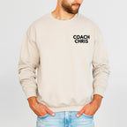 Beige sweatshirt with 'COACH CHRIS' text worn by a person on a light gray background