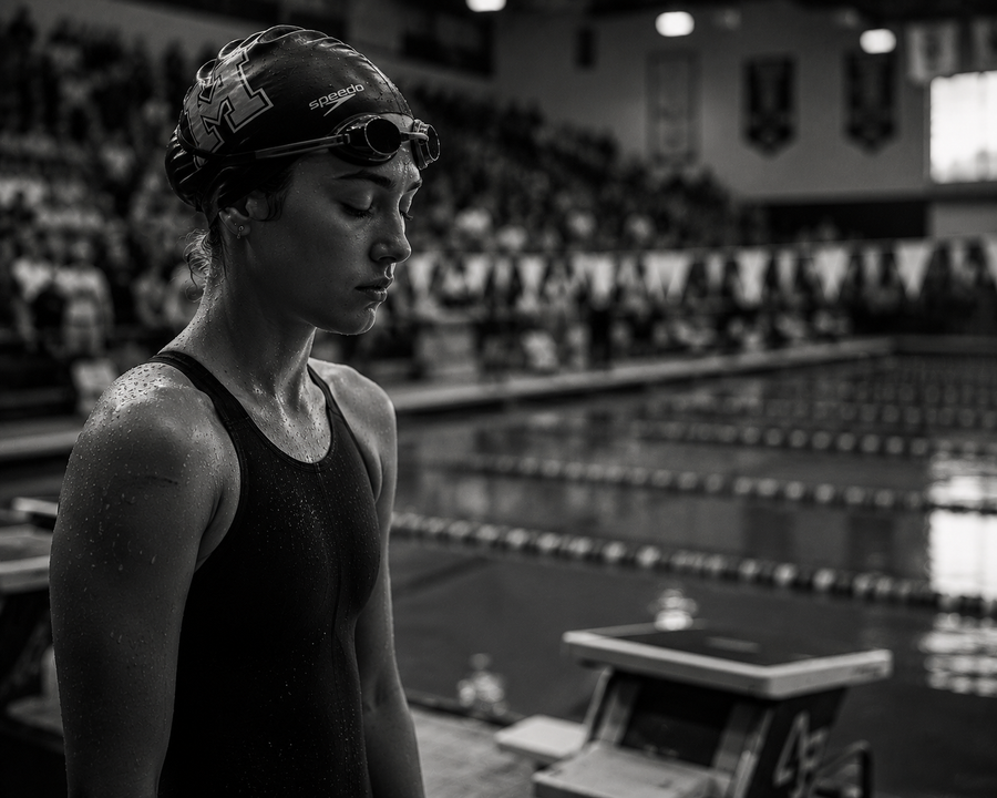 Black and white photo of a swimmer standing by the poolside with a swim cap and goggles on.